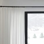 White curtains partially covering a window with a snowy outdoor view. Minimalist home decor.
