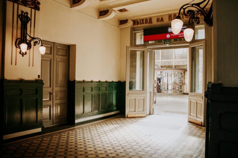 Elegant vintage hallway with intricate lighting and open door leading to an outdoor view.